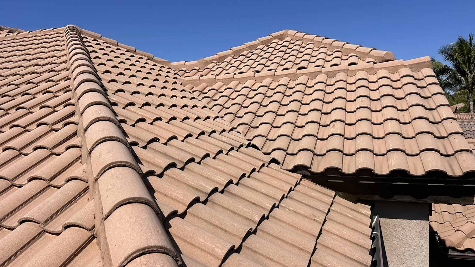 Close-up view of a residential home’s tan tile roof showing overlapping curved clay tiles against a blue sky.