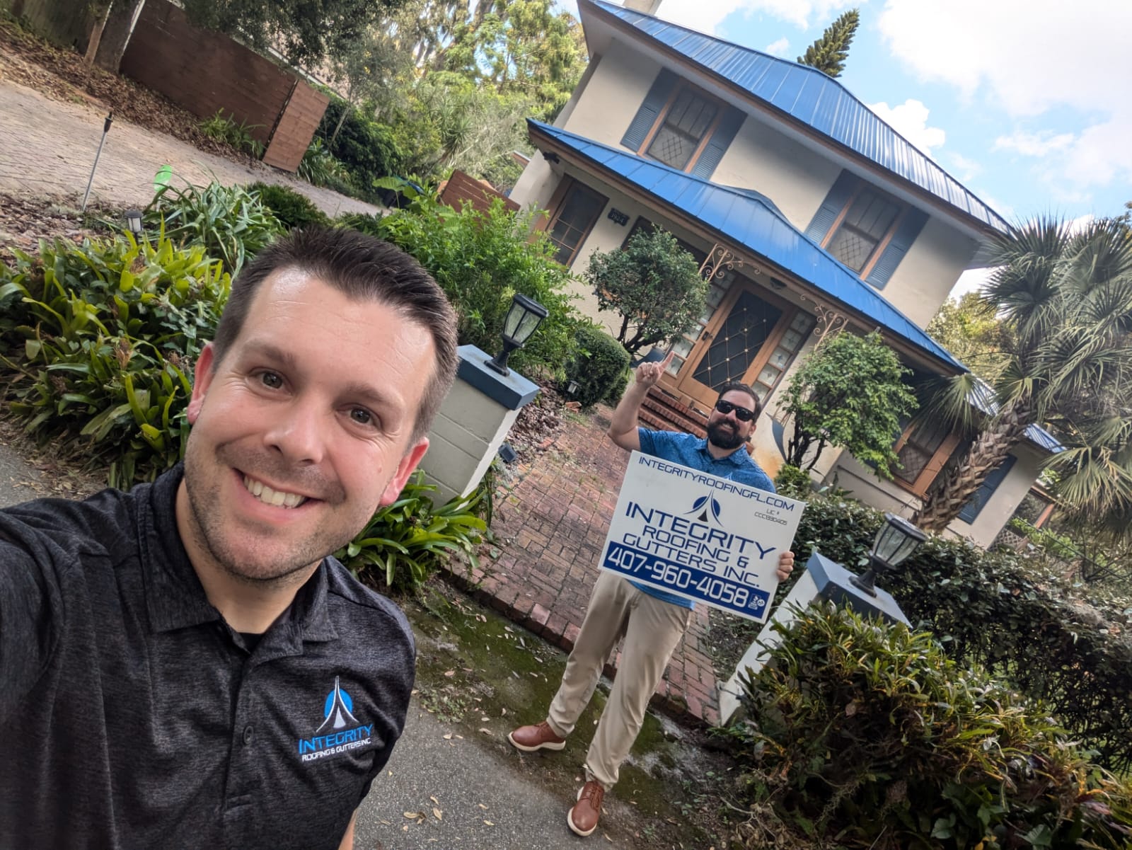 Integrity Roofing & Gutters team members standing in front of a Florida home with a newly installed blue metal roof, holding a company sign after completing a residential roof replacement.
